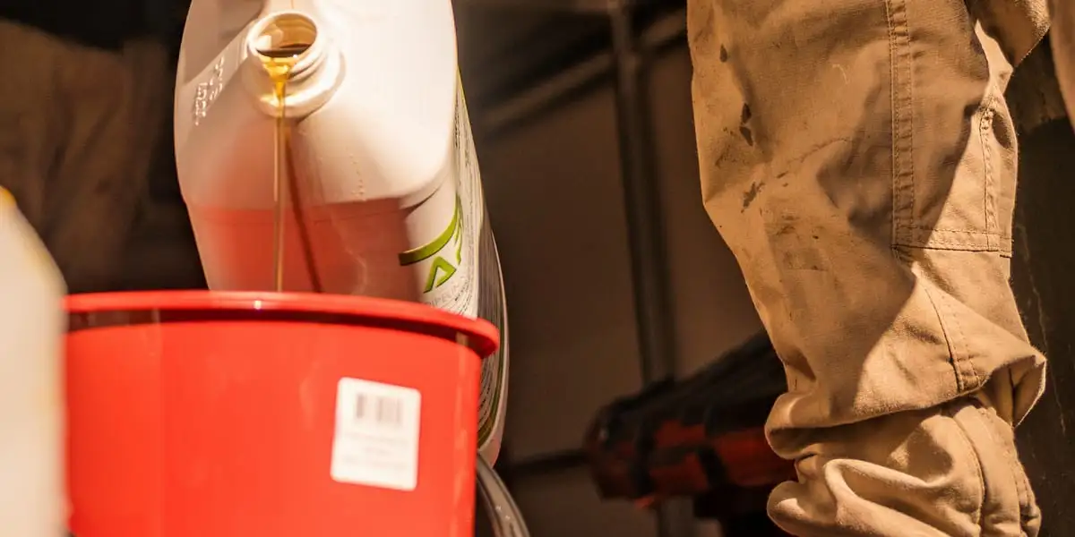 Amber resin running from a plastic container into a red mixing tub in the back of the work truck, with the technician standing over it in dust-covered work trousers.